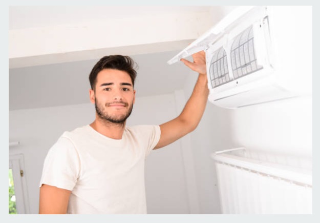 Un homme se tient devant une bouche de climatisation avec le sourire à son installation réussi par les équipes de PAC Eco