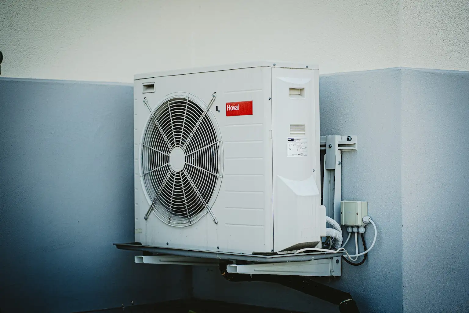 Bloc de climatisation externe installé dans le coin d'un batiment et surélevé du sol. installation par PAC éco